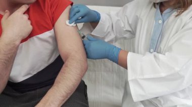 Doktorun elleri çok yakın. Doktor kişiye bir enjeksiyon yapar. Mevsimlik aşı. İnokülasyon. Coronavirüs.