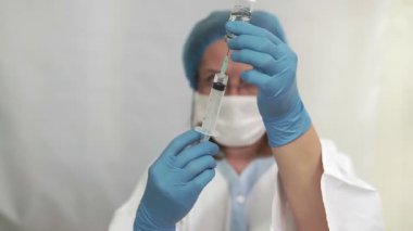 Doktor aşıyı şırıngaya koyar. Cam şişe bir teknisyenin elinde. Tedavisi olan bir şişe silikon eldivenlerde el tutar. Tedavide bir atılım. Aşı muayeneleri. Salgın.