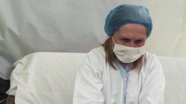 Maskeli bir kadın doktor ofiste koronavirüs üzerinde çalışıyor. Covid-19 simgesi.