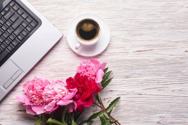 Kadın ofis masası dümdüz uzanıyordu. Dizüstü bilgisayarı olan bir kadın çalışma alanı, pembe şakayık buketi ve beyaz arka planda kahve. Üst görünüm kadınsı arkaplan.