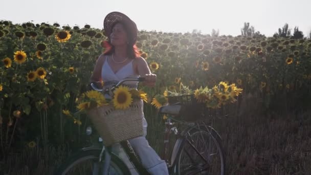 一个头戴帽子 身穿白色衣服 骑自行车的女人带着向日葵在花粉中穿行 — 图库视频影像
