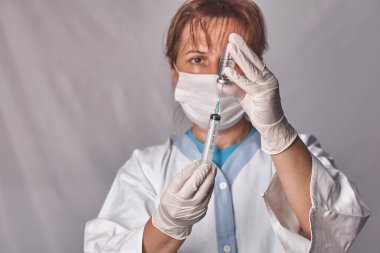 Doktor aşıyı şırıngaya koyar. Cam şişe bir teknisyenin elinde. Tedavisi olan bir şişe silikon eldivenlerde el tutar. Tedavide bir atılım. Aşı muayeneleri. Salgın.