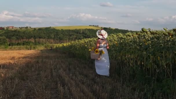 一个头戴帽子 身穿白衣的女人站在开着向日葵的田里 — 图库视频影像