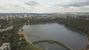 Sonbahar ağaçlarıyla dolu bir parktaki göl manzarası. Kishinev, Moldova. Suyun üzerinde destansı bir uçuş. Gündüz vakti renkli sonbahar ağaçları. Drone sarı ağaçlı bir göl boyunca uçar. 4K İHA Atışı.