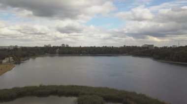 Sonbahar ağaçlarıyla dolu bir parktaki göl manzarası. Kishinev, Moldova. Suyun üzerinde destansı bir uçuş. Gündüz vakti renkli sonbahar ağaçları. Drone sarı ağaçlı bir göl boyunca uçar. 4K İHA Atışı.