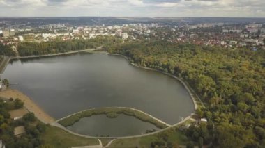 Sonbahar ağaçlarıyla dolu bir parktaki göl manzarası. Kishinev, Moldova. Suyun üzerinde destansı bir uçuş. Gündüz vakti renkli sonbahar ağaçları. Drone sarı ağaçlı bir göl boyunca uçar. 4K İHA Atışı.