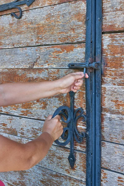 女性は錬鉄製の要素で飾られた古代の木製のドアを開きます 鉄のハンドル付きの古いロック 接近中だ 選択的焦点 — ストック写真