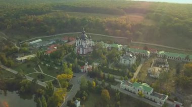 Günbatımında sonbahar ormanlarıyla çevrili bir Hıristiyan manastırının üzerinden uçmak. Kurky Manastırı, Moldova Cumhuriyeti.