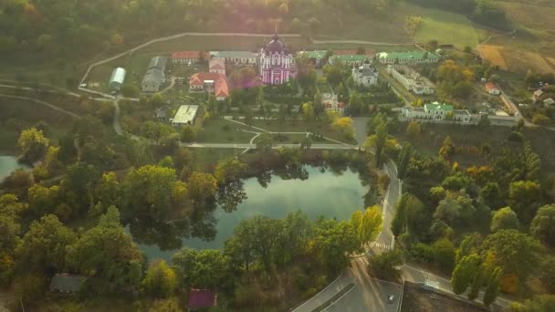 Günbatımında sonbahar ormanlarıyla çevrili bir Hıristiyan manastırının üzerinden uçmak. Kurky Manastırı, Moldova Cumhuriyeti. — Stok video