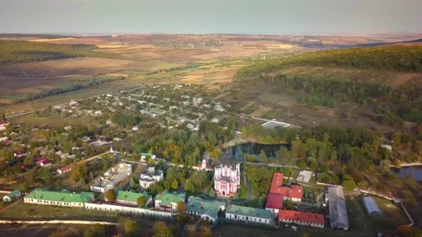日没の秋の森に囲まれたキリスト教の修道院の上を飛行します モルドバ共和国クルキー修道院 — ストック動画