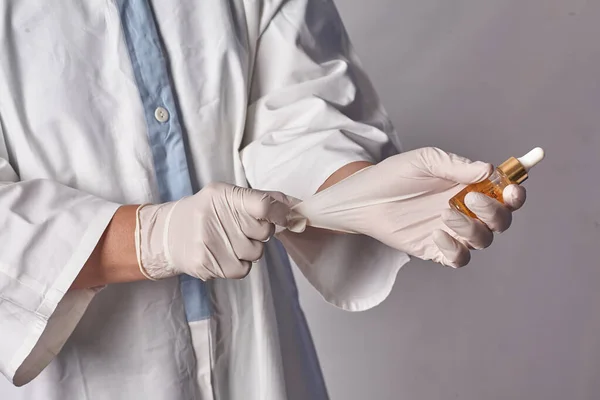 Proteger a los trabajadores sanitarios de la infección. Una doctora se pone guantes médicos sobre un fondo blanco aislado y sonríe. Equipos de protección individual antes del examen de los pacientes —  Fotos de Stock