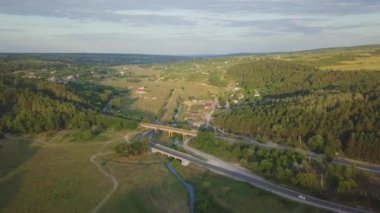 Güneşli bir yaz gününde yeşil tarlaların arasından geçen karayolu üzerindeki hava manzarası. Çayır ve kırsal alan arasında asfalt çevre yolu olan 4K manzara görüntüsü. Drone video çekiyor.