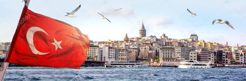 Panorama of Istanbul with Galata Tower at skyline and seagulls over the sea, wide landscape of Golden Horn with the Turkish flag in the foreground, travel background for billboard