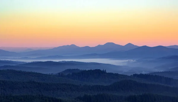 Foggy matin dans les montagnes avec des silhouettes de collines. Sérénité lever de soleil avec lumière douce du soleil et des couches de brume. Paysage de montagne avec brume en bois aux couleurs pastel — Photo