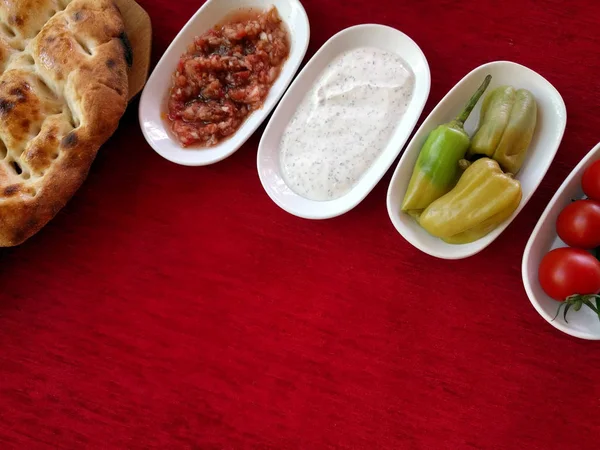 Pan, verduras, salsas y aperitivos en platos sobre un mantel rojo, vista superior con espacio de copia vacío, fondo para el menú — Foto de Stock