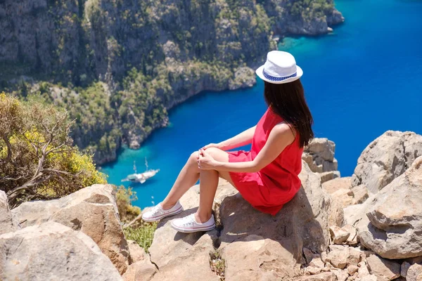 Paisaje Oludeniz, Turquía, una joven con un vestido rojo mira el Valle de la Mariposa desde arriba, sentada sobre las rocas —  Fotos de Stock