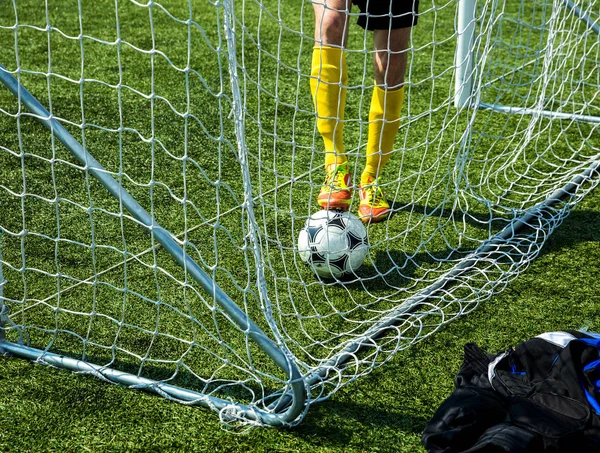 Soccer Ball in the grid of gate, the team player pulls the scored the ball out of the goal on green field