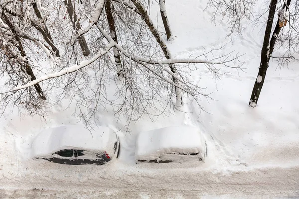 Cars covered with snow in the parking in the yard near a house. View from the top