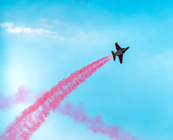 Silhouette sport aircraft with propellers, performing tricks with a red smokescreen against the blue sky in the air show performance