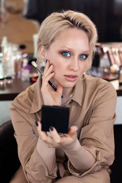 Güzellik salonunda makyaj fırçası ve pudrası olan güzel sarışın bir kadının yakın plan portresi.