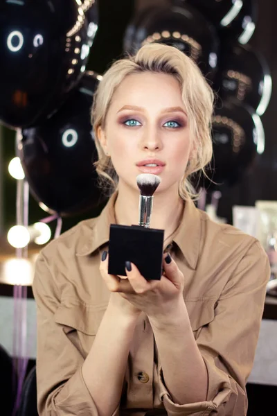 Güzellik salonunda makyaj fırçası ve pudrası olan güzel sarışın bir kadının yakın plan portresi.