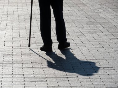 Baston, uzun gölge kaldırımda yürüyen aksak adam silüeti. Engellilik, yaşlılık, kör kişi, dramatik yaşam konsepti