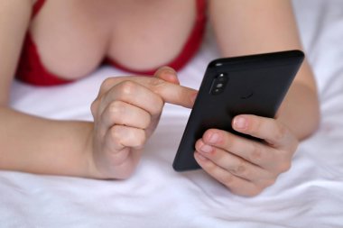 Seksi kadın yatakta yatıyordu ve smartphone kullanarak iç çamaşırı. Eller, Internet, online iletişim, sms, sosyal medya, zina, ev gevşeme kavramı içinde hareket eden telefon