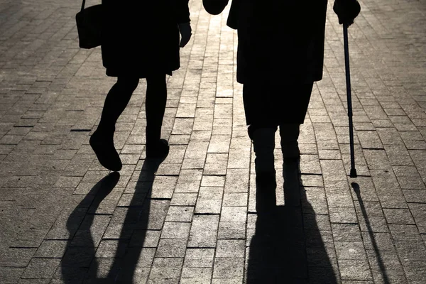 Girl and woman with a cane, black silhouettes and shadows of two people walking on the street. Concept of limping, old age, elderly or blind person