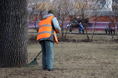 Şehirdeki yaprakları temizliyor, kapıcı kadın bahar parkındaki yaprakları süpürüyor. Moskova 'da sokak temizleyicisi, konut ve kamu hizmetleri.