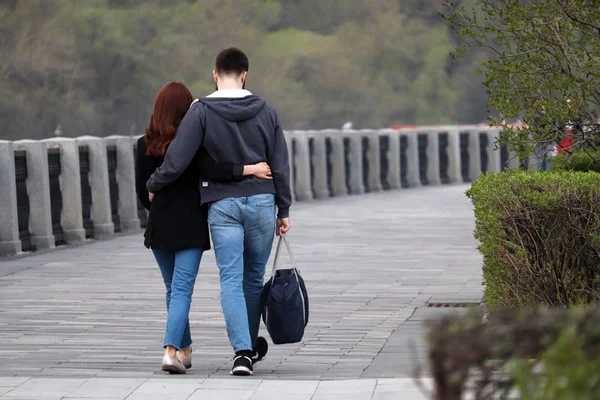 Aşık çift sarılma ve bir parkta yürüyüş, arka görünümü. Romantik bir tarihte erkek ve kız kucaklayan, kot pantolon insanlar, ilişki kavramı, gerçek duygular, şehirde bahar sezonu