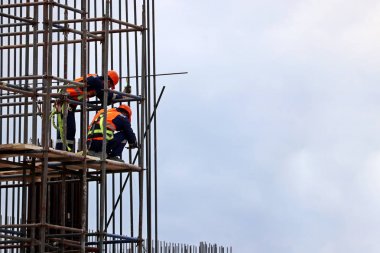 İskele üzerinde çalışan inşaat işçileri. Mavi gökyüzüne karşı bina çerçevesi üzerinde Yükleyiciler