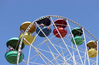 Berrak mavi gökyüzü arka plan üzerinde renkli kabin ile dönme dolap. İnsanlar lunaparkta lanet çarka biniyor.