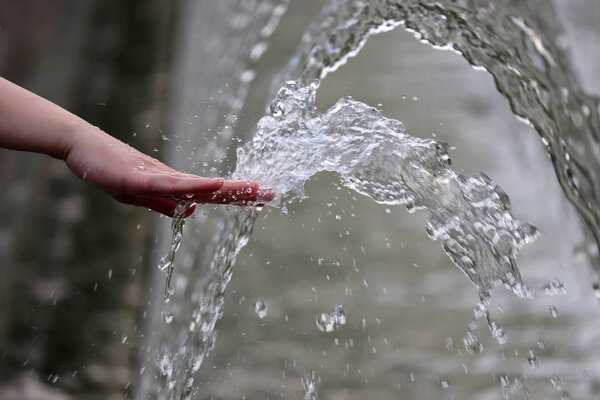 Freshness and cool, female hand in a water of the fountain. Girl playing with splashing jets, concept of humidity, hot summer weather