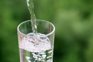 Yeşil doğa arka plan üzerinde içme cam içine temiz su dökme. Sağlık ve tazelik kavramı, susuzluk, su arıtma ve ekoloji