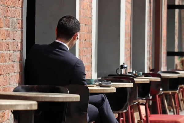 Stylish man in a business suit sitting at a table in street cafe. Concept of lunch alone, waiting for a date or business meeting, coffee break