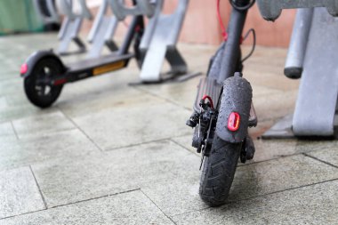 Yağmur sırasında otoparkta elektrikli scooterlar, tekerlekte su damlaları. Şehirde yağmurlu hava, bisiklet kiralama sistemi