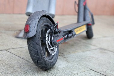 Yağmur sırasında otoparkta elektrikli scooter, tekerlekte su damlaları. Şehirde yağmurlu hava, bisiklet kiralama sistemi
