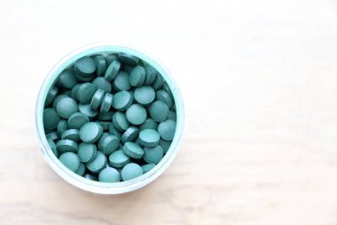 Beyaz ahşap masada bir şişede Spirulina ve Chlorella tabletler. Sağlık için beslenme takviyeleri, üst görünüm