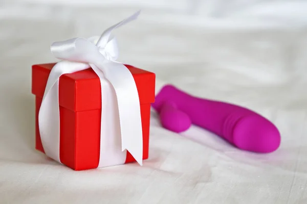 Red gift box and dildo on a bed, romantic present for adult. Purple silicone vibrator, sex toy for Valentine's day