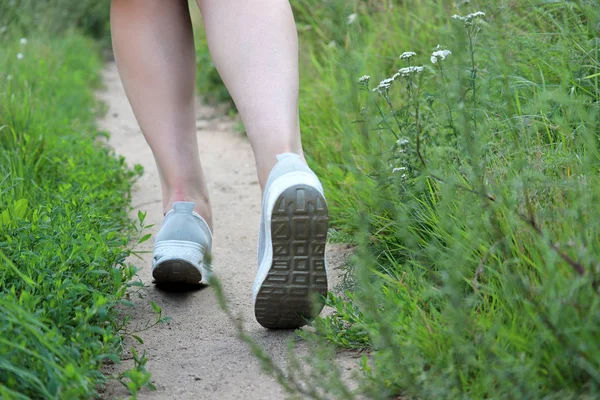 緑の草の中の小道を走る女の子 女性の足がクローズアップ ワークアウトのコンセプト 女性ランナー 夏季のスリミング — ストック写真