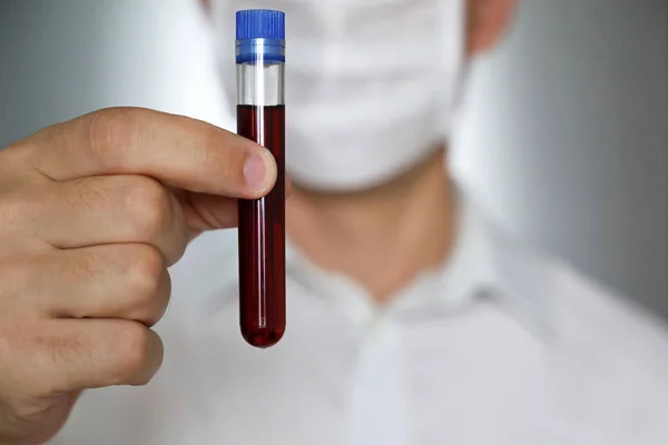 Man in medical mask with a test tube in his hand. Concept of blood sample, doctor, scientist, medical research