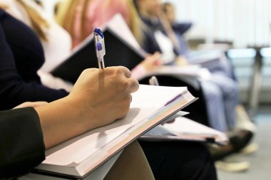 Bir konferans odasında üst üste oturan kadınlar, not defterine kalem yazan kadın elleri. Ders kavramı, iş toplantısı, üniversite dersleri, beceri geliştirme, personel eğitimi
