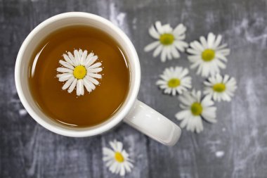 Beyaz bir fincan papatya çayı ve koyu ahşap bir masada papatya çiçekleri, şifa bitkisel içecek