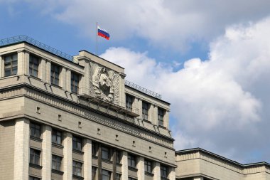 Moskova'daki parlamento binasında mavi gökyüzü ve beyaz bulutların arka planında Rus bayrağı. Sovyet arması ile Rusya Devlet Duma Cephesi, Rus otoritesi