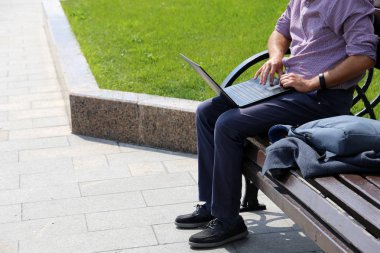 Yeşil çim arka plan üzerinde bir yaz şehirde bir bankta bir dizüstü bilgisayar ile oturan adam. Klavyede erkek elleri, işadamı kavramı, açık havada çalışma, çevrimiçi iletişim