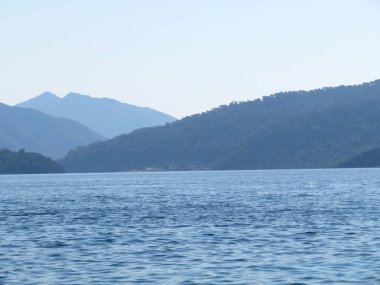 Sabahları denizden dağlık adalara, sahile bak. Pitoresk deniz manzarası, dağlar ve tepeler ile kıyı şeridi bir sis, narin mavi renk güzel panorama orman kaplı