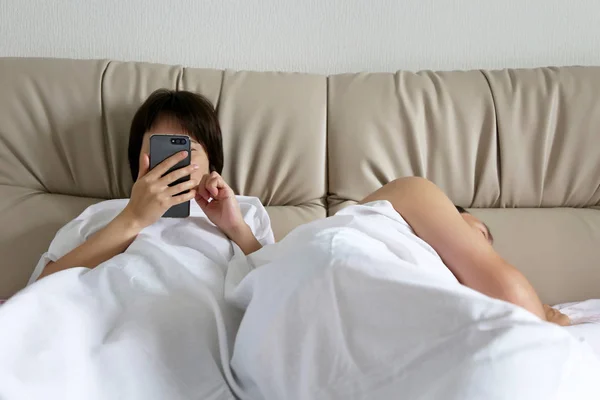 Wife using smartphone in a bed for texting while her husband is sleeping. Concept of family issues, adultery, sex dating, online addiction