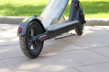 Yeşil çimenlik yakınındaki bir otoparkta elektrikli scooter. Çevre dostu ulaşım, şehir kiralama sistemi, bir sokakta e-scooter