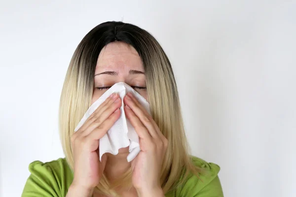 Sick woman sneezing in a handkerchief. Blonde girl with eyes closed on white background, concept of colds and flu, runny nose, airborne infection