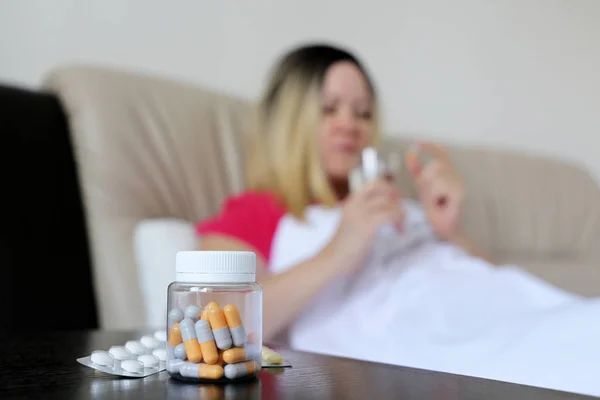 Cold and flu season, pills and capsules in bottle on background of sick woman lying and taking medication in a bed. Concept of illness, fever, hot temperature